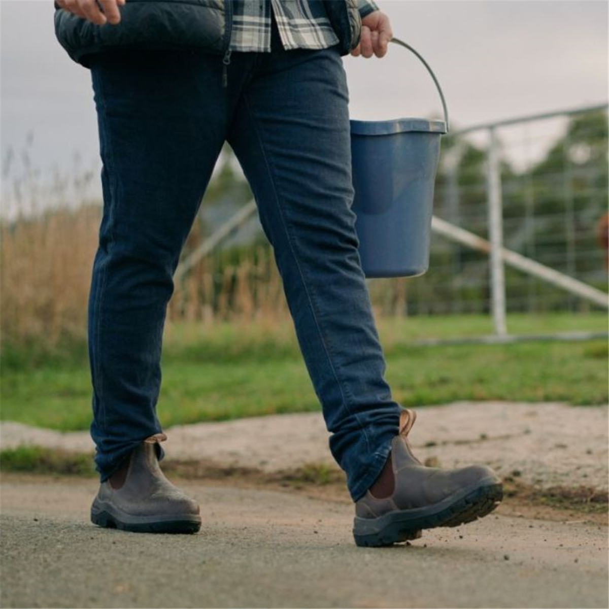 Side view of Blundstone 710 Chelsea work boots being worn with blue jeans while walking outdoors on a farm path