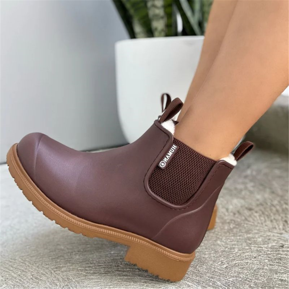 Brown rubber boot with a brand logo on a neutral background