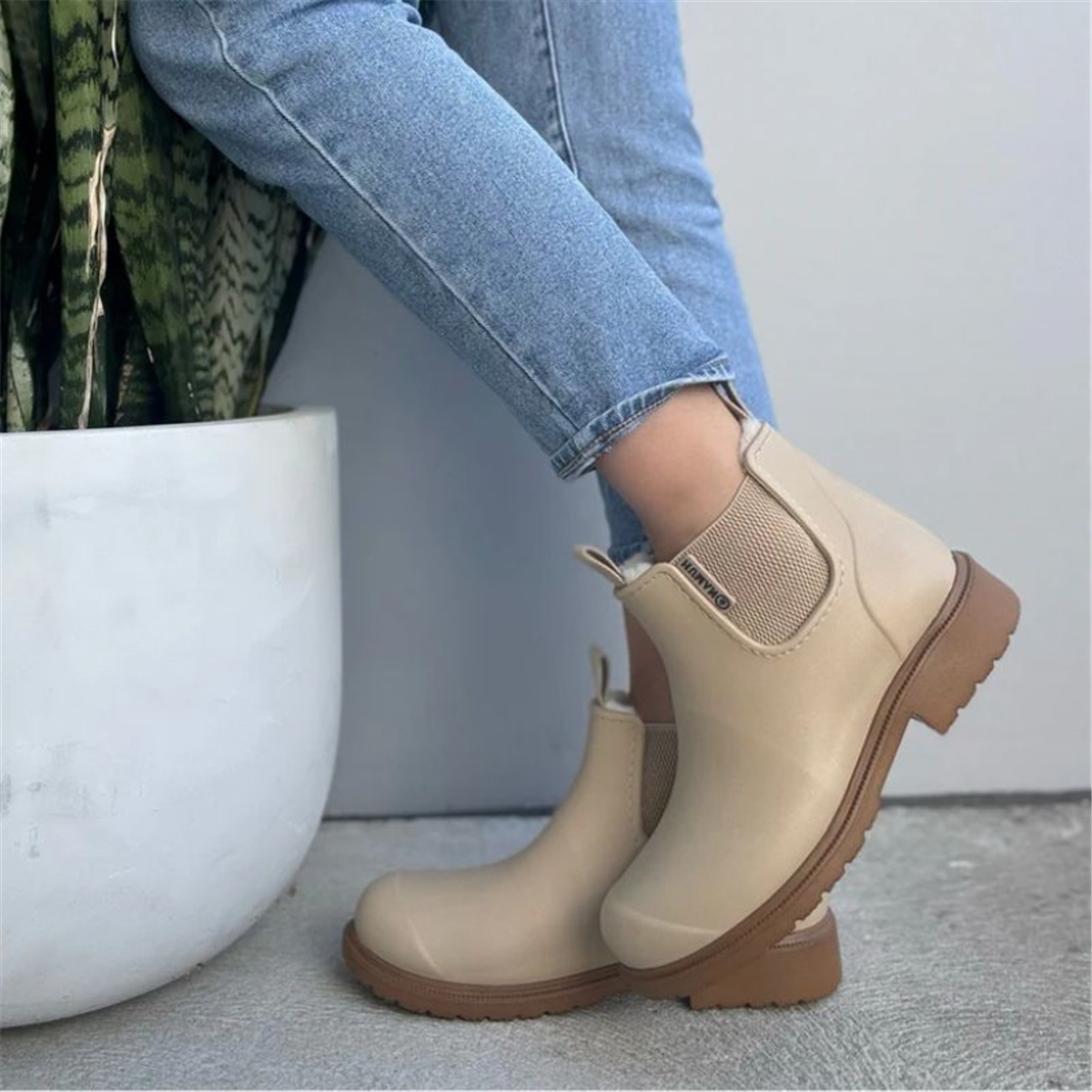 Beige rubber boots worn with blue jeans on a light gray background